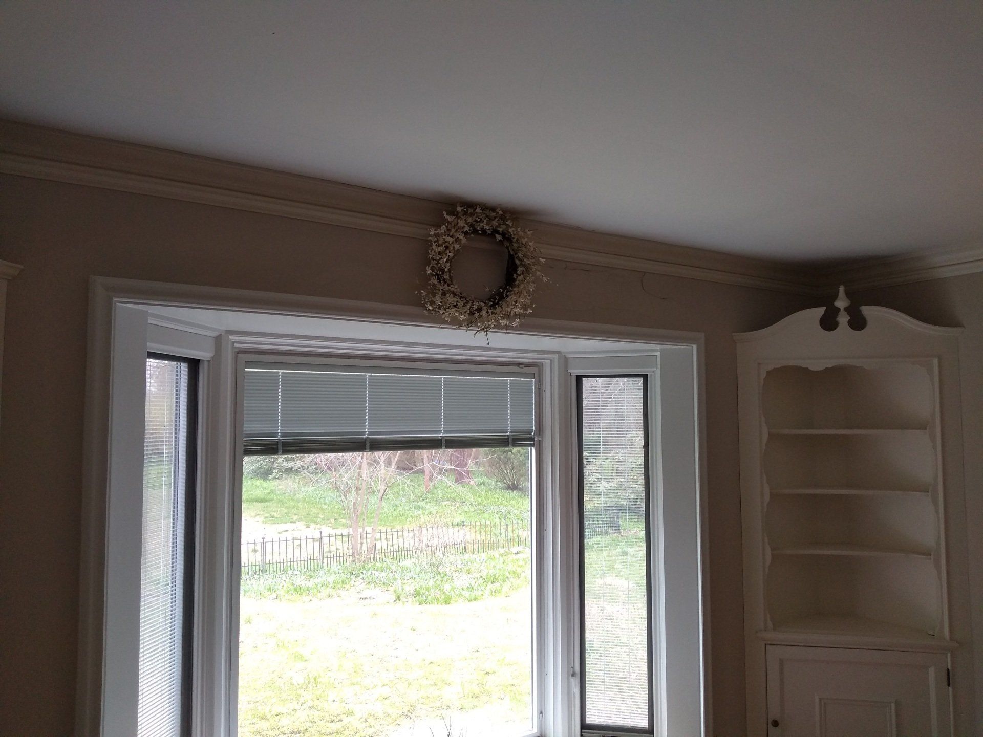A living room with a bay window and a wreath on the ceiling.