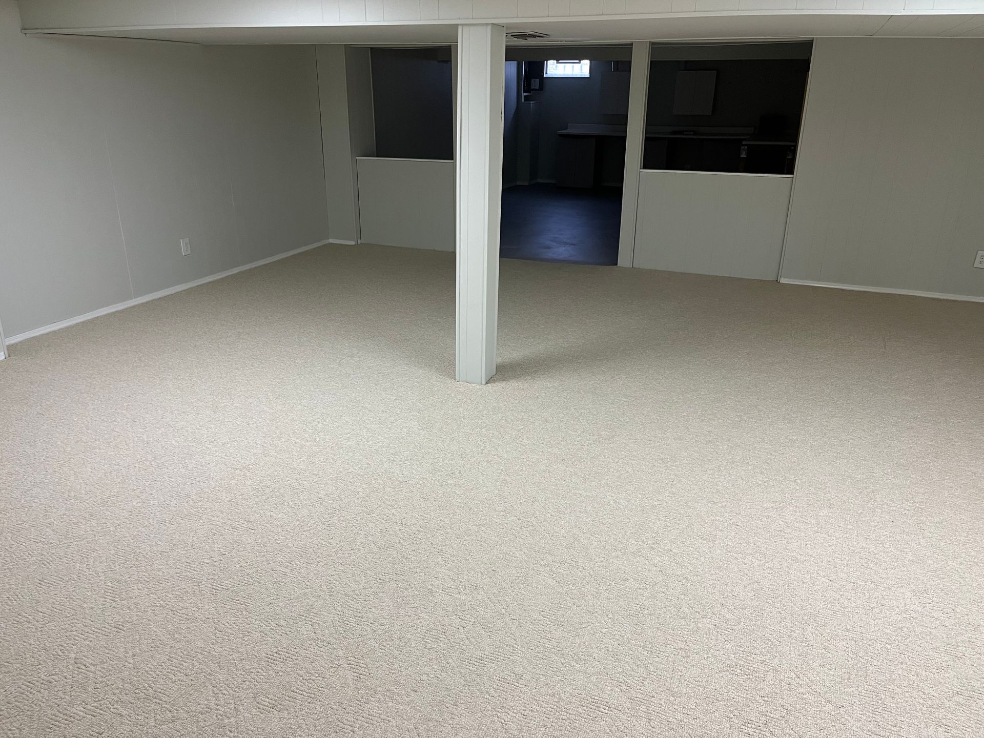 An empty basement with a carpeted floor and a pillar.