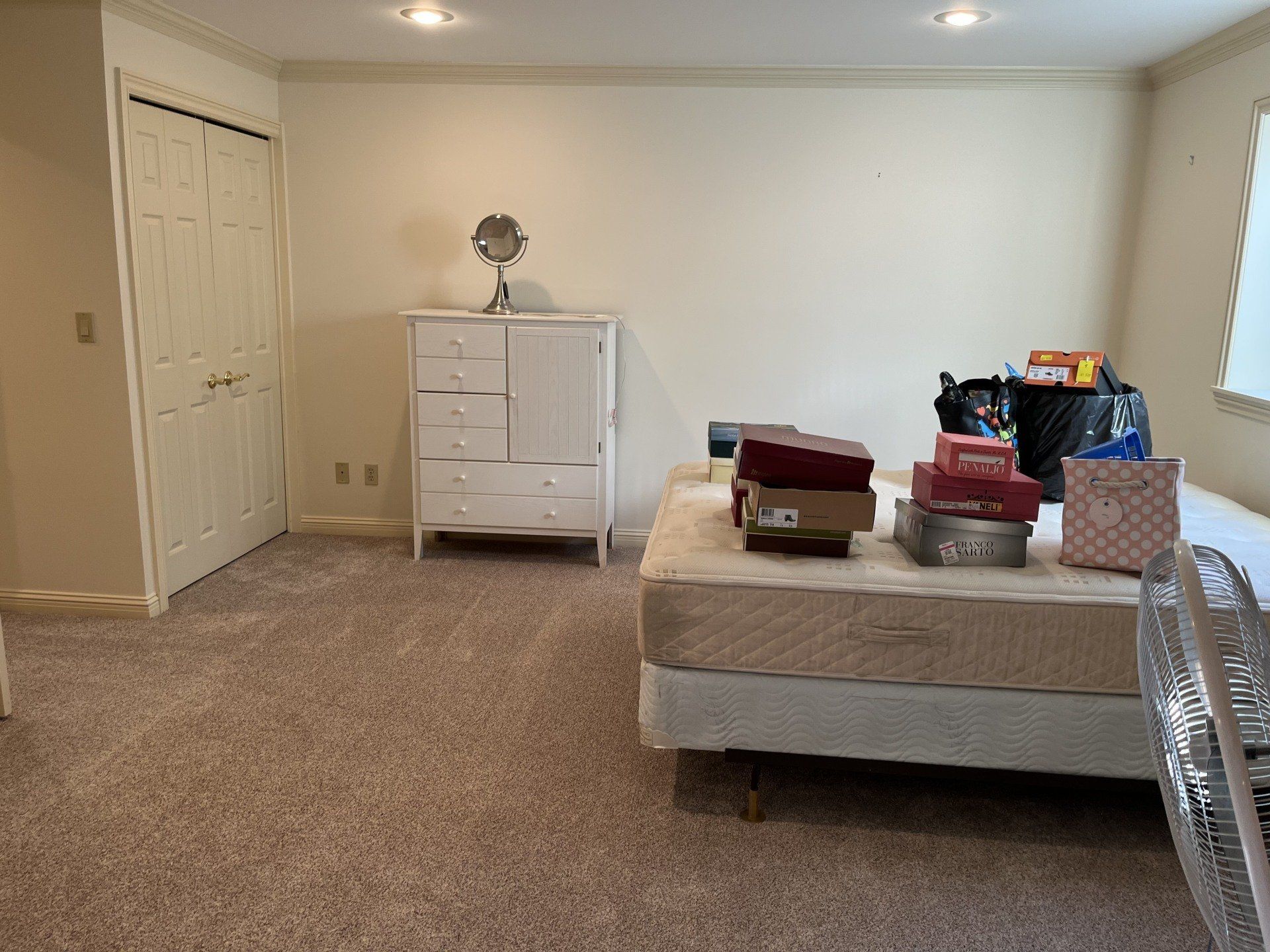 A bedroom with a bed , dresser , mirror and fan.