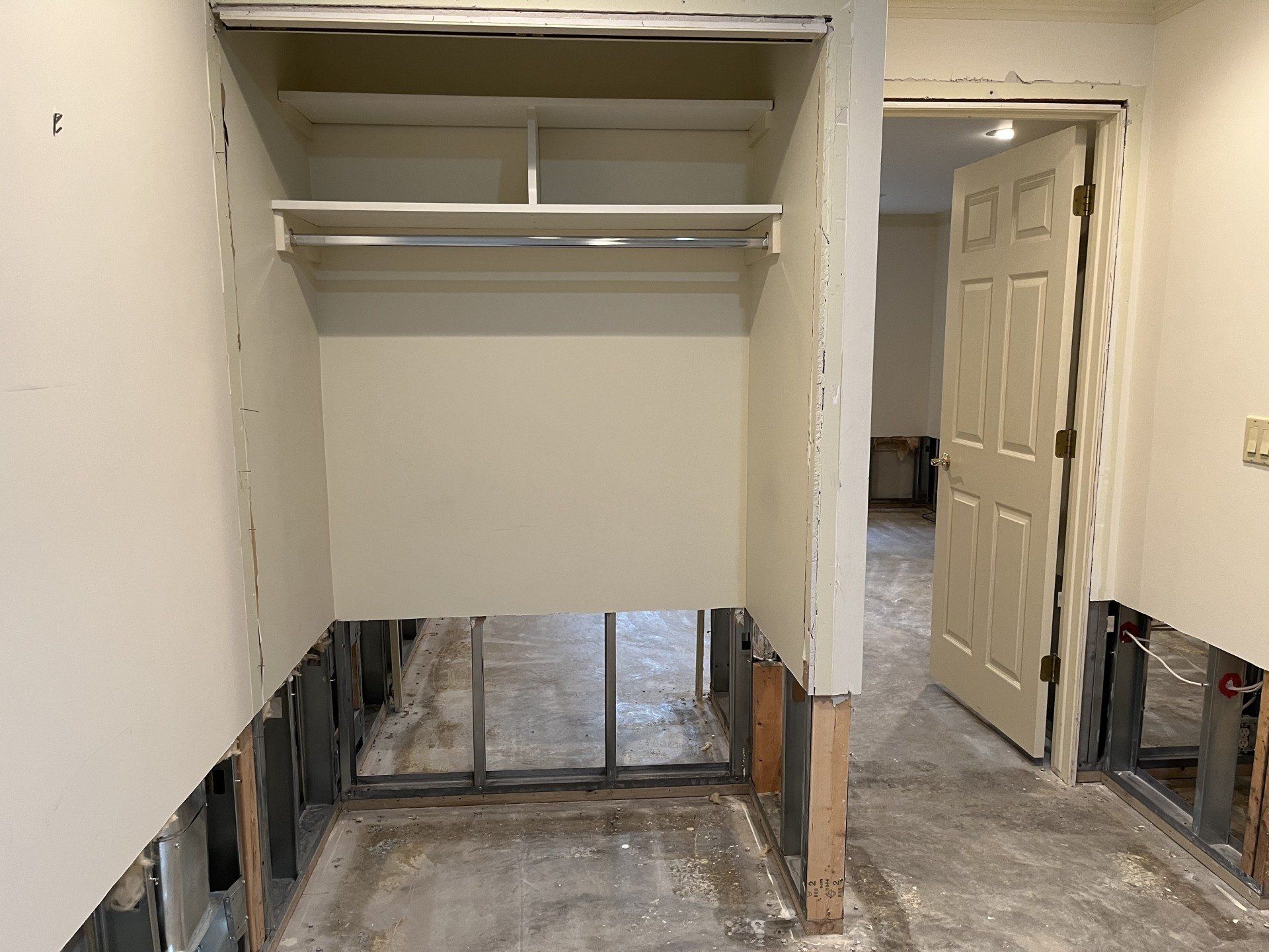 A closet with a shelf and a door in a house under construction.