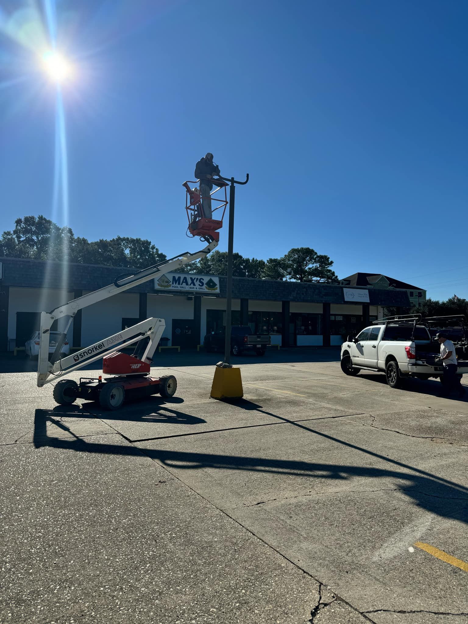 A man is working on a light pole in a parking lot.