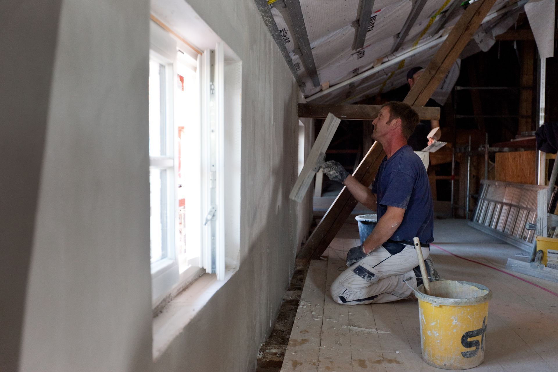 Ein Mann kniet auf einem Dachboden und streicht eine Wand.