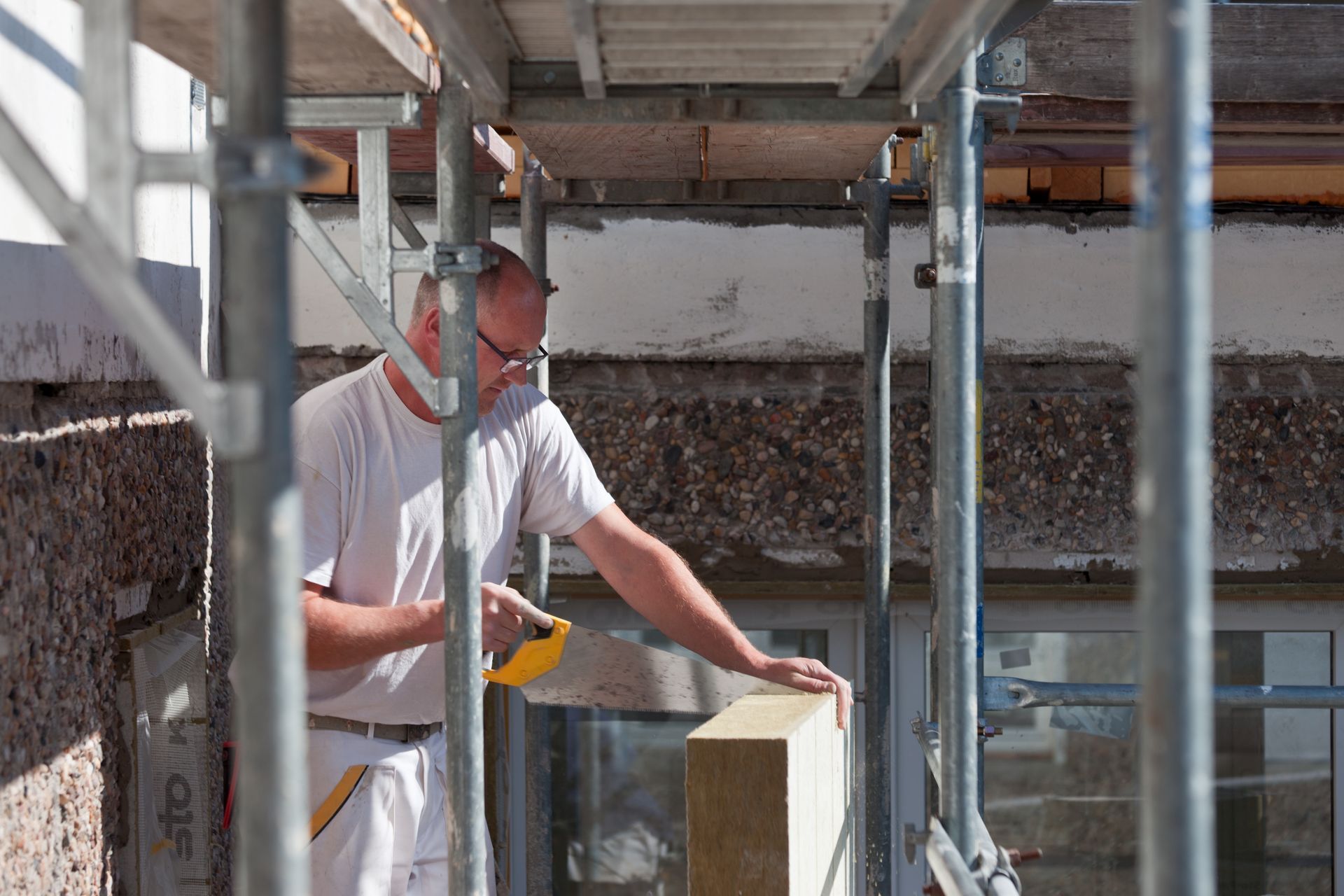 Ein Mann misst ein Stück Holz auf einem Gerüst.