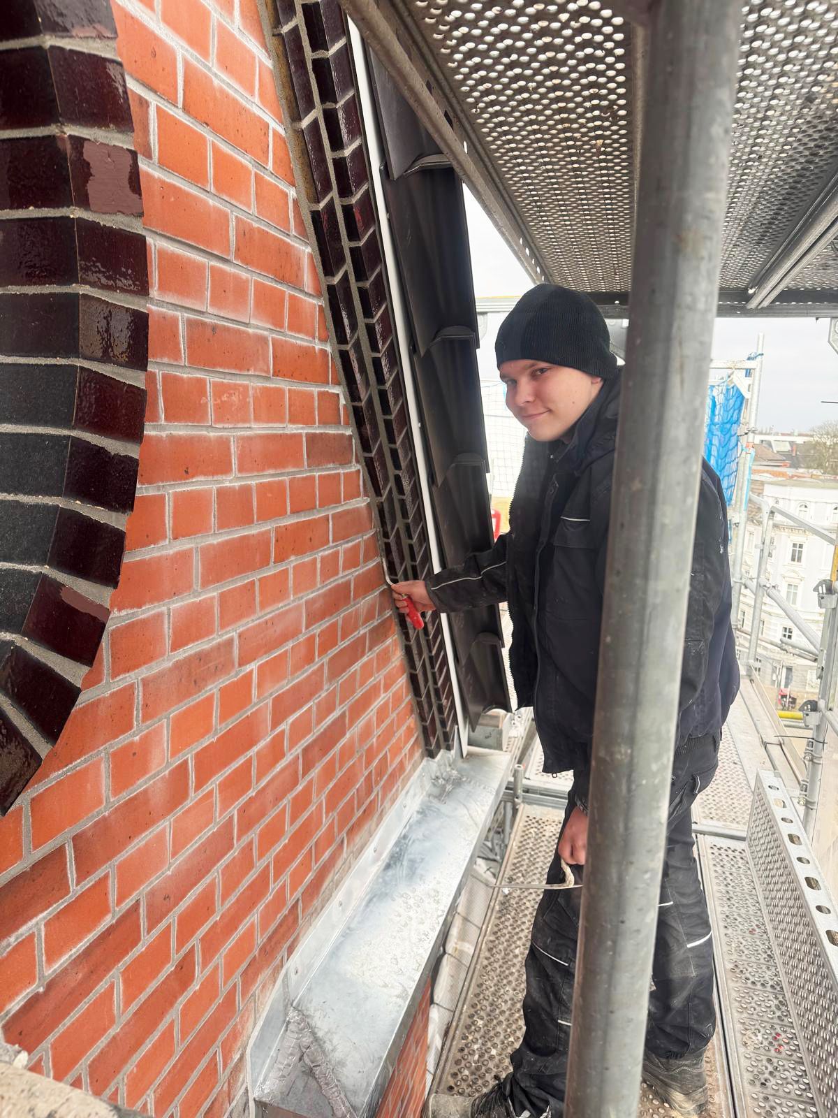 Ein Mann in Arbeitskleidung arbeitet auf einem Gerüst an einer Fassade.