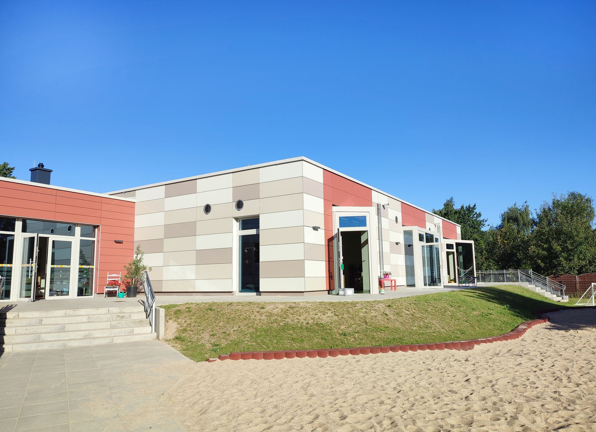 Ein Kita-Gebaeude mit Glastueren und Sandflaeche davor