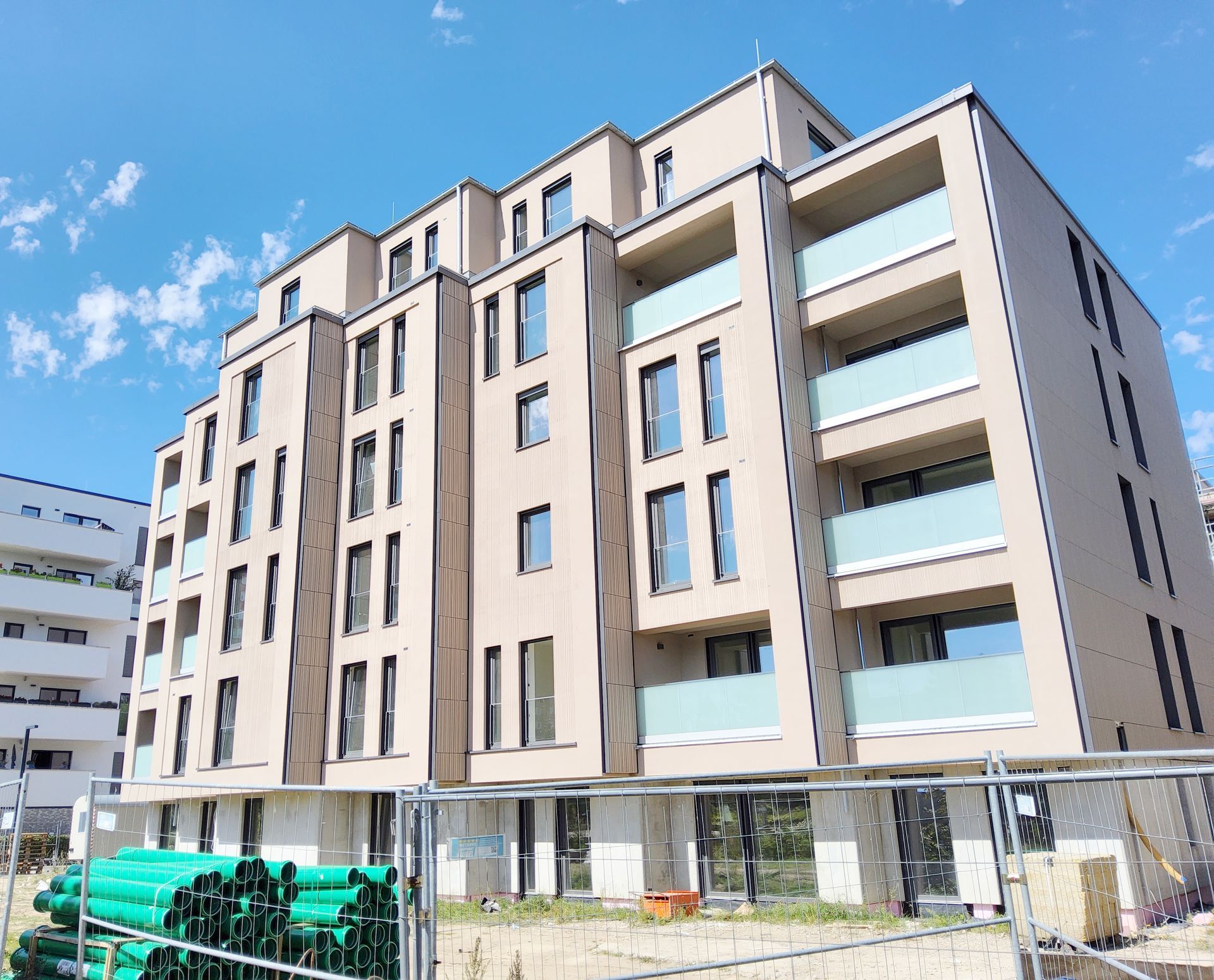 Ein großes Mehrfamilienhaus mit interessanter Architektur und einem Bauzaun und Rohren davor.