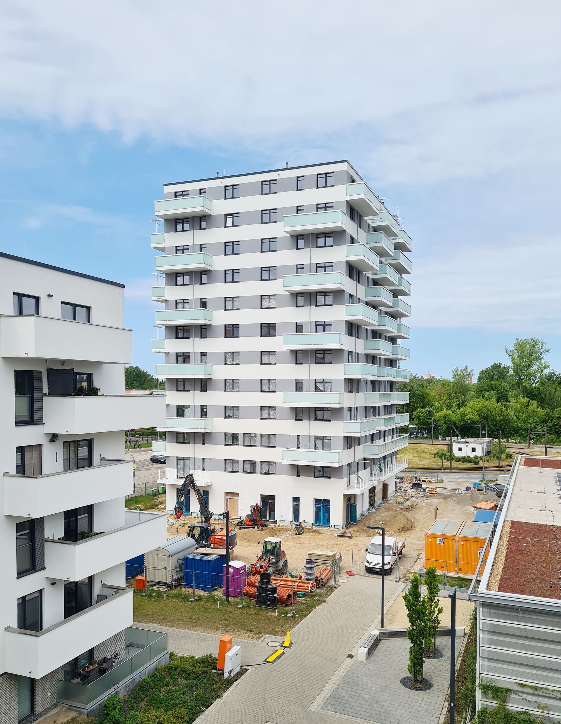 Ein modernes, neugebautes Mehrfamilienhaus mit Balkonen und 11 Stockwerken inmitten einer Baustelle.