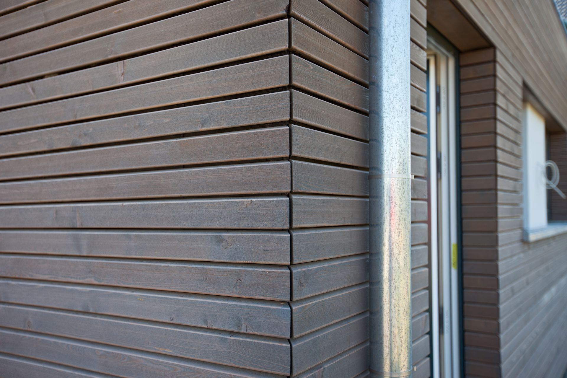 Eine Ecke eines Gebäudes mit Holzverkleidung und einem Metallrohr