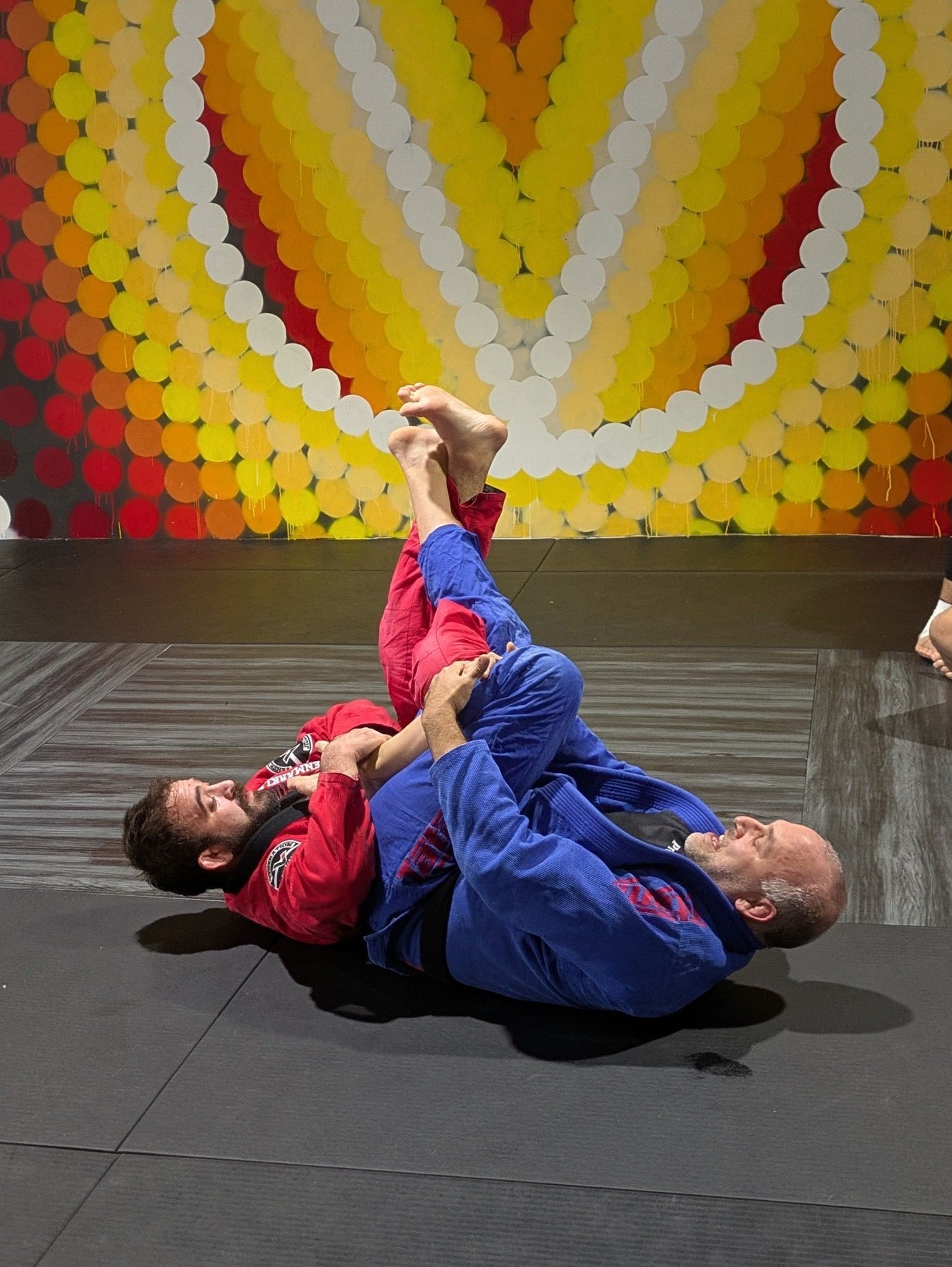 Two men are wrestling on a mat in front of a colorful wall