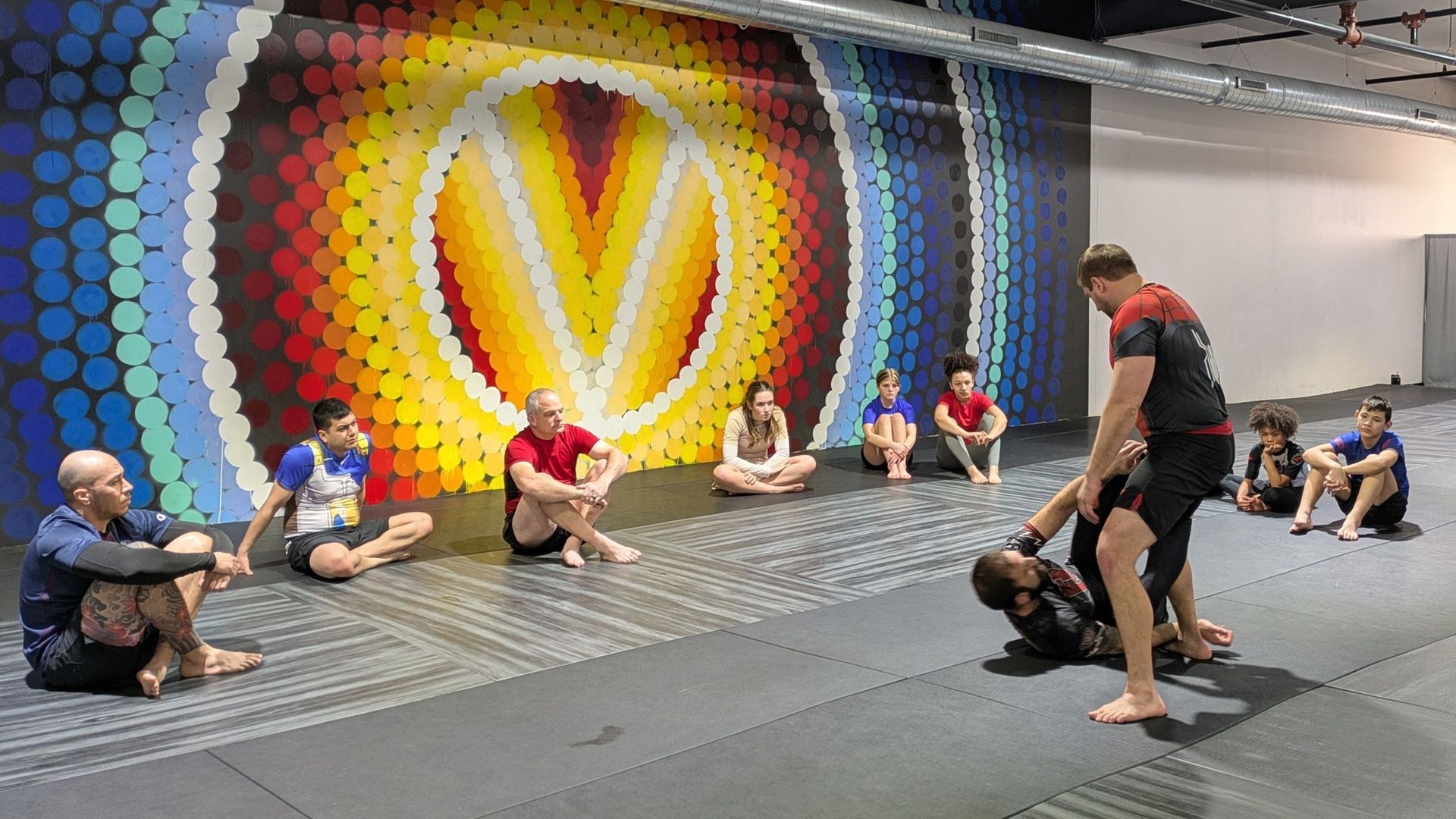A group of people are sitting on the floor in a gym.