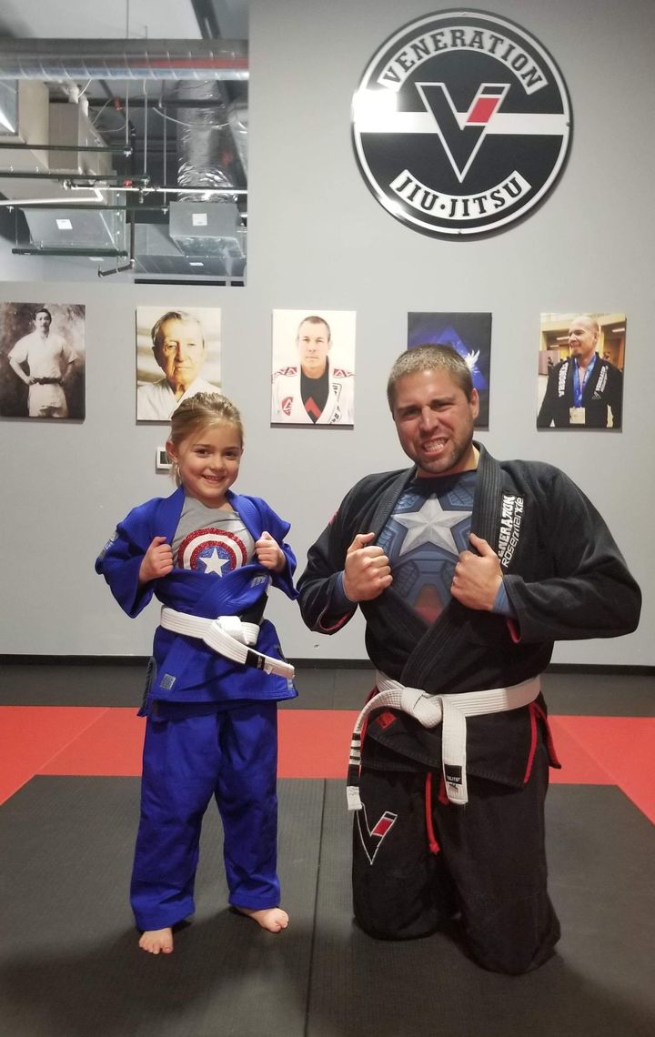 A man and a little girl are posing for a picture in front of a sign that says jiu-jitsu