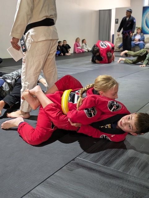 A boy and a girl are wrestling on a mat in a gym.