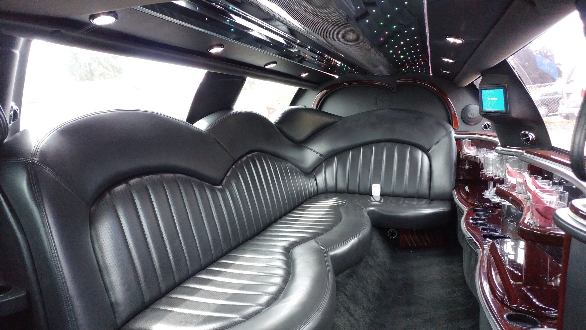 The inside of a limousine with black leather seats and a bar.