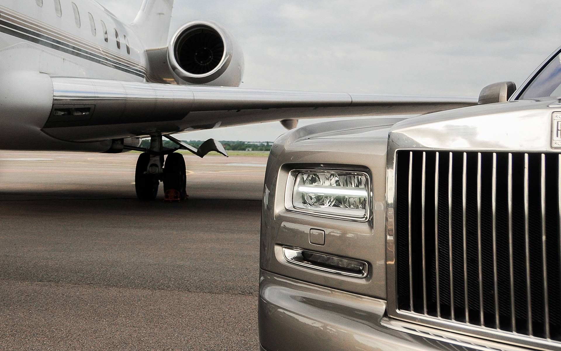 A rolls royce car is parked next to a private jet on a runway.