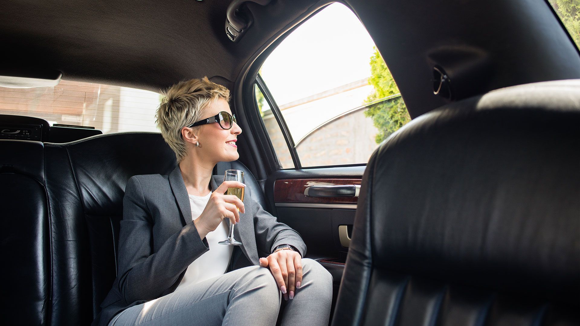 A woman is sitting in the back seat of a limousine holding a glass of champagne.
