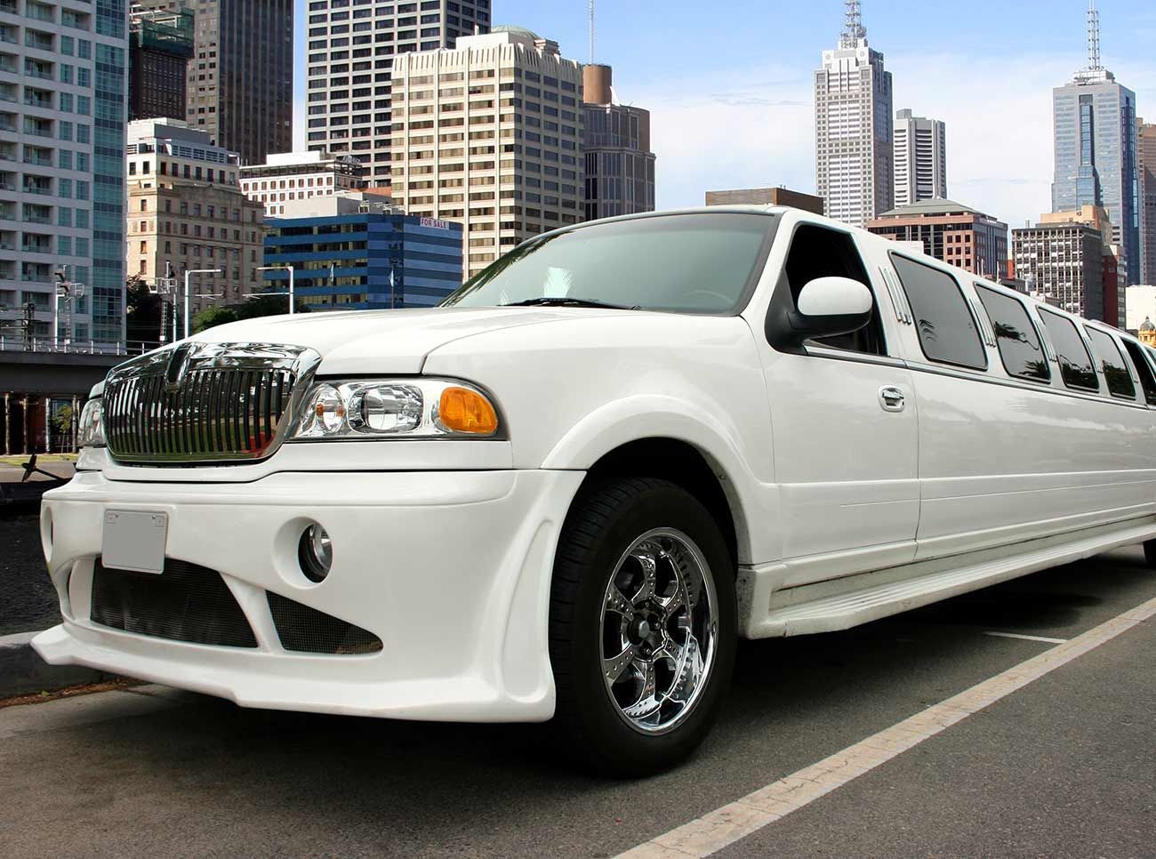 A white limousine is parked in front of a city skyline.