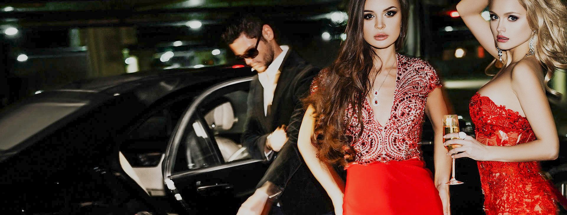 A man in a tuxedo is standing next to two women in red dresses.