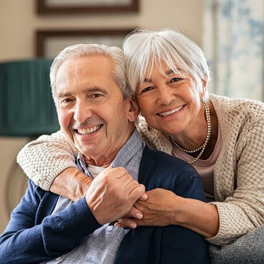 A woman is hugging an older man on a couch.