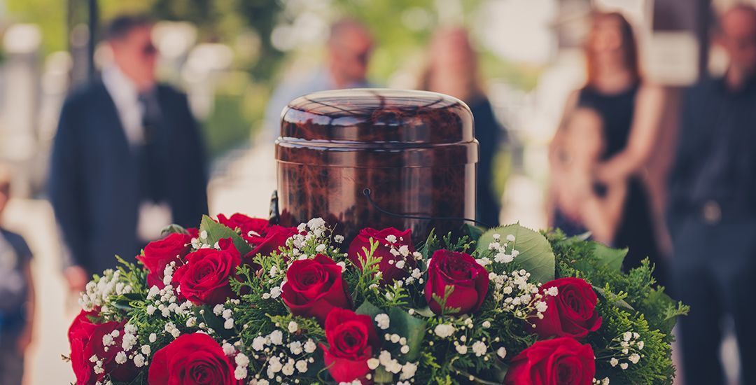 An urn is surrounded by red roses and baby breath at a funeral.