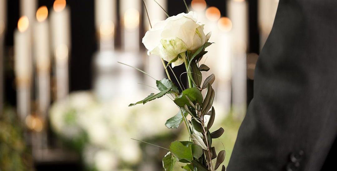 a man in a suit is holding a white rose at a funeral.