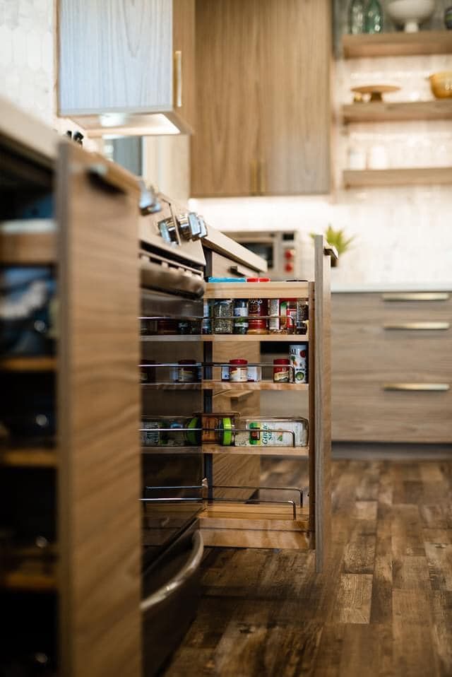 Wooden kitchen with open cabinet showcasing spice rack and oven.