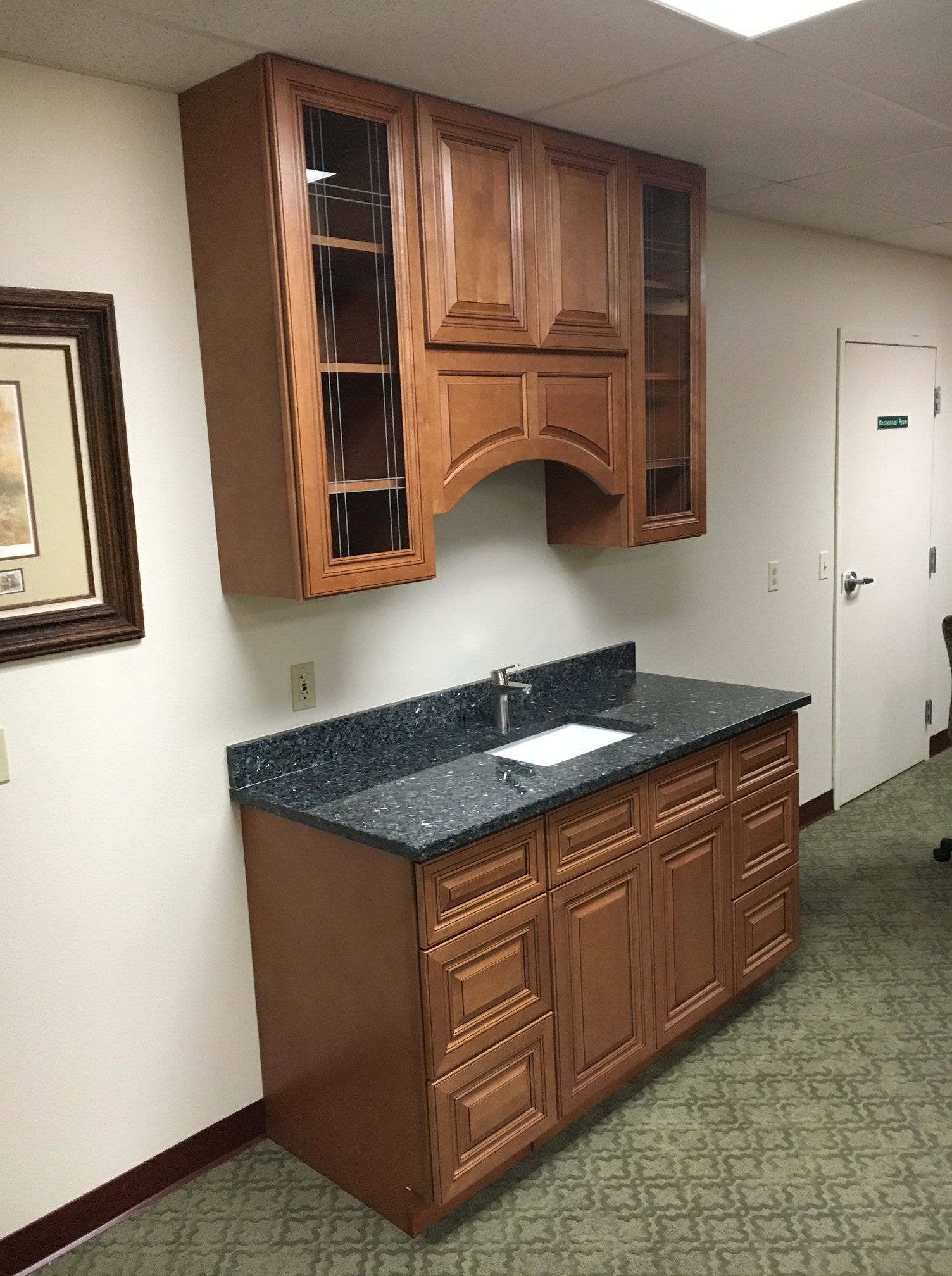 A wall-mounted cabinet and counter with a sink, drawers, and upper cabinets. The countertop is dark.