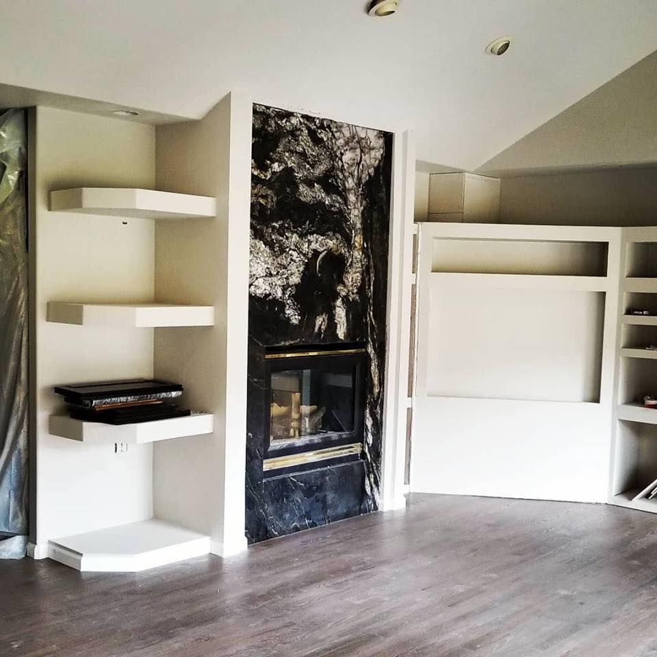 Empty room with fireplace, shelves, and built-in storage. Dark stone fireplace surround and wood floors.