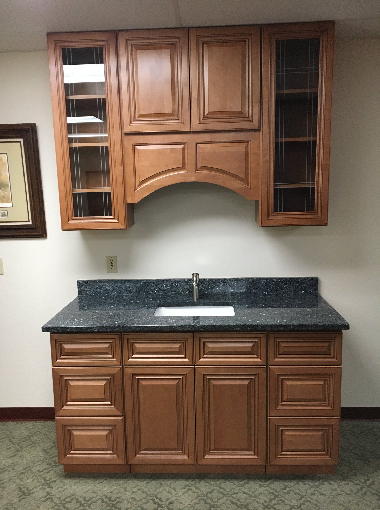Brown wooden bar with granite countertop and cabinets, including upper storage and a sink.