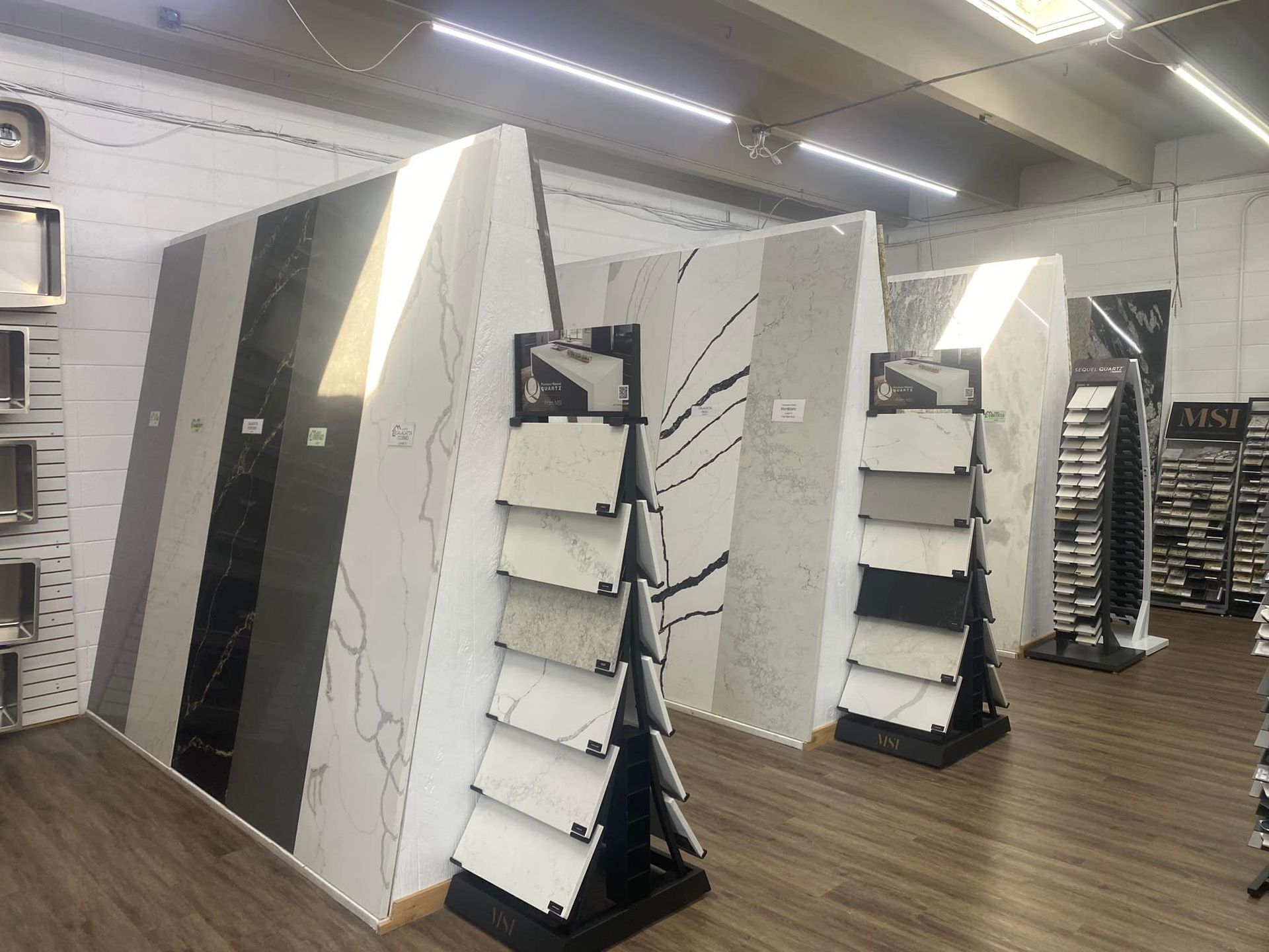Samples of stone slabs and tile displays in a showroom with wood flooring and overhead lighting.