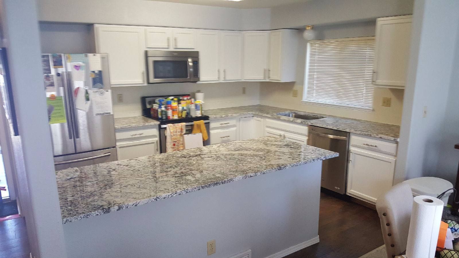 White kitchen with granite countertops, stainless steel appliances, and dark wood floors.