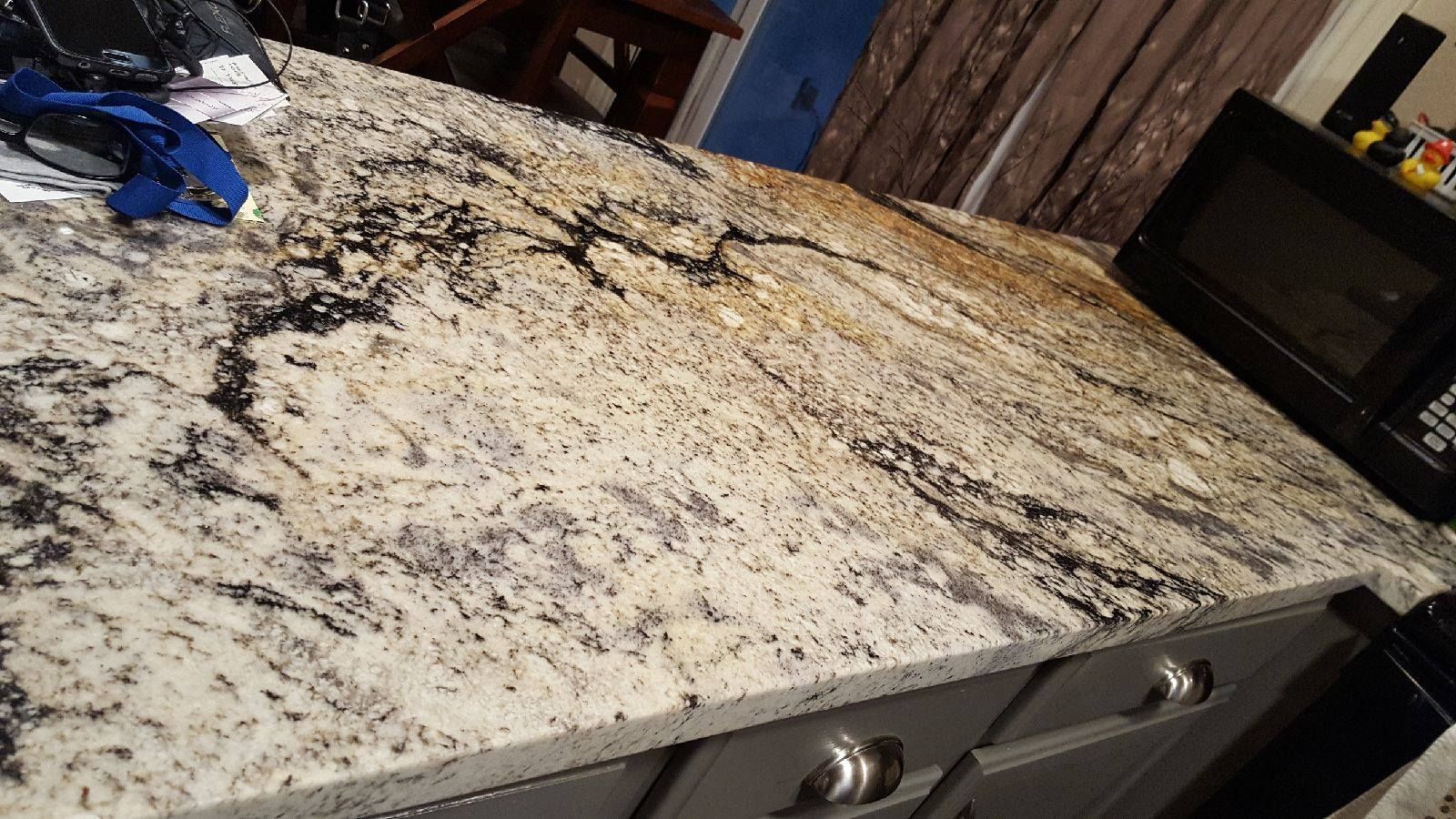 Granite countertop with black and gold veining, next to a black oven and gray cabinets.