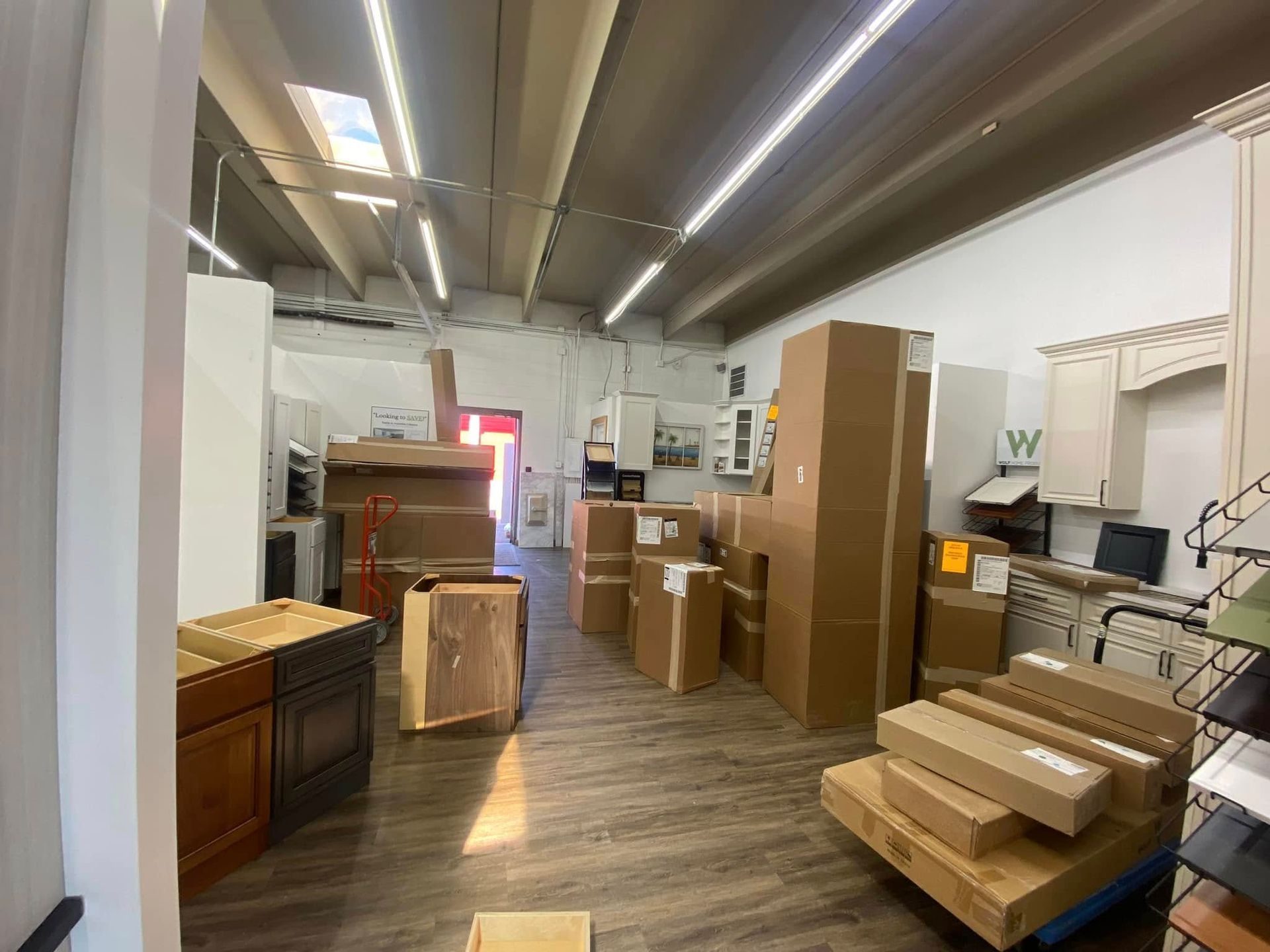 Interior of a store, cabinets and boxes stacked.  Exposed ceiling, wood-look floor, doorway, and side display.