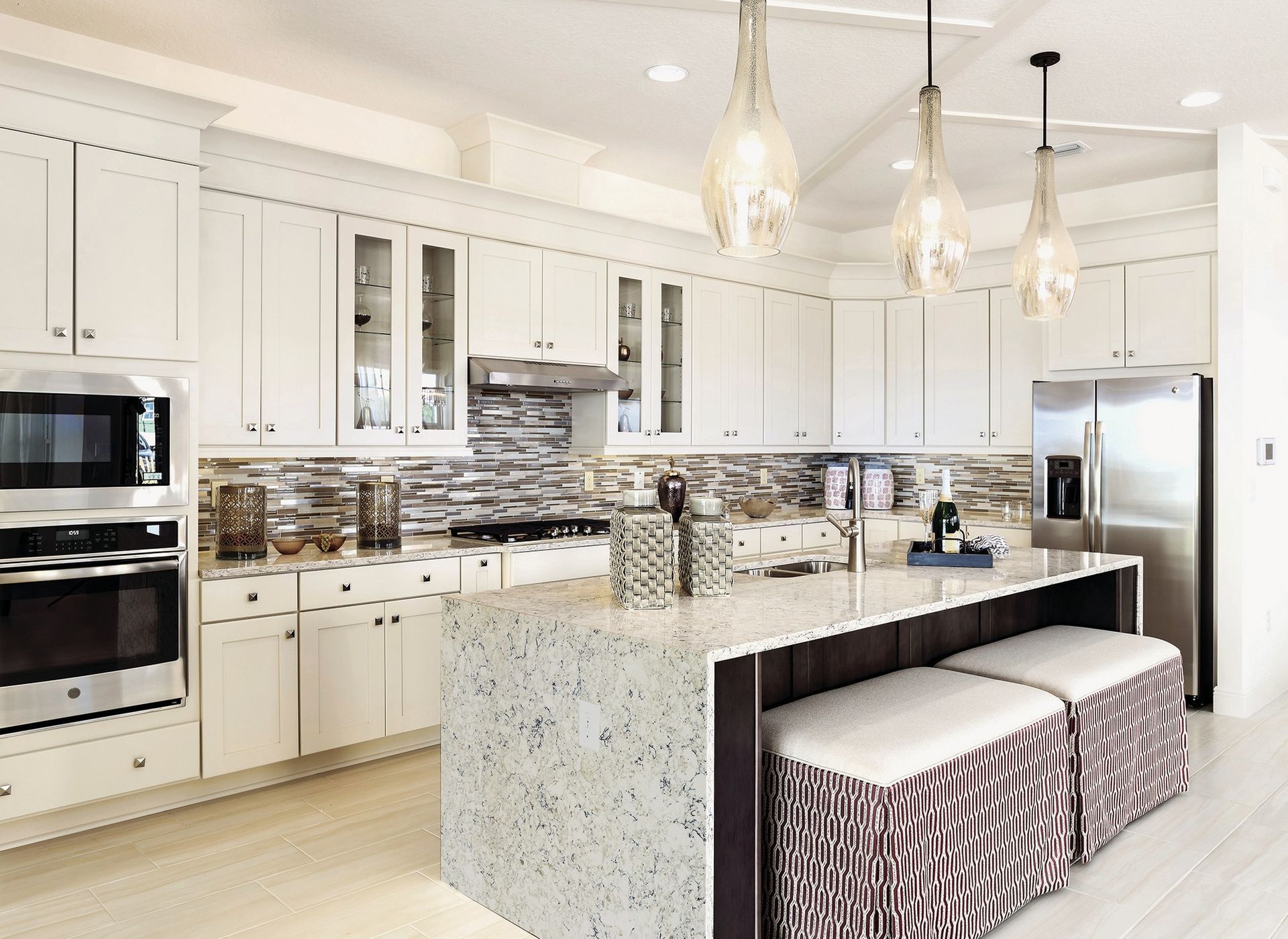 White kitchen with island, cabinets, stainless steel appliances, and pendant lights.