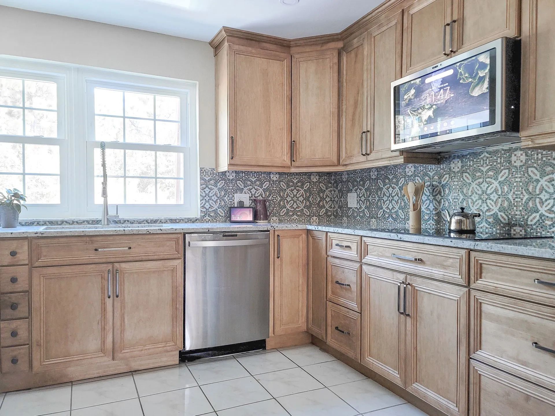 Bright kitchen with wood cabinets, tiled backsplash, stainless dishwasher, window, and light tile floor