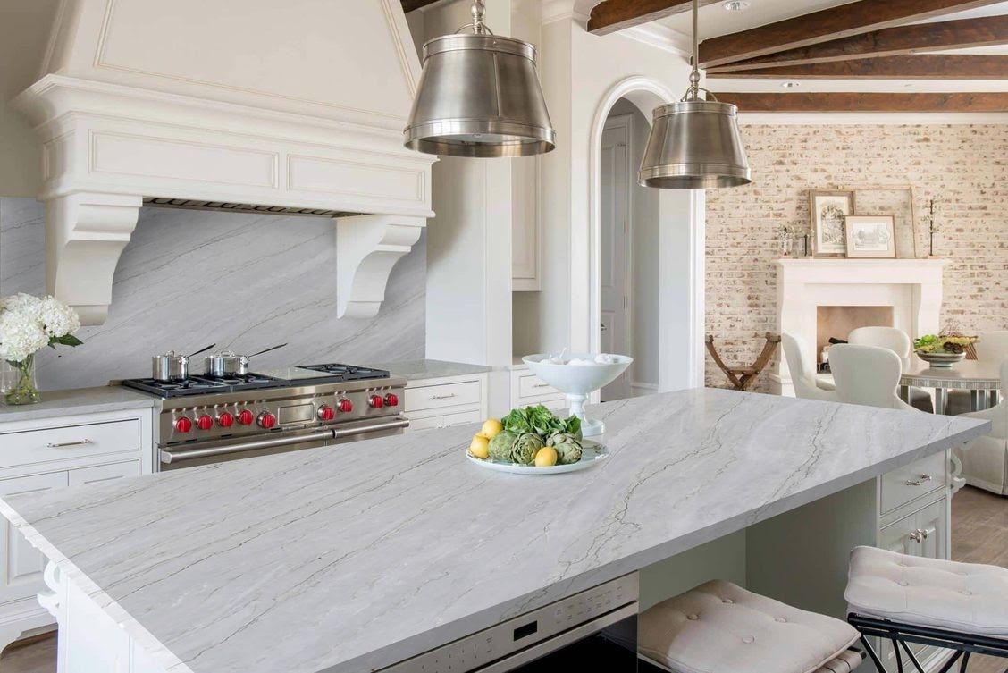 Elegant white kitchen with island, range, and hood. Stainless steel pendant lights hang above.
