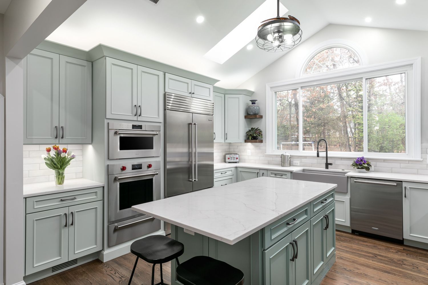 Light blue kitchen with island and stainless steel appliances; window in the background.