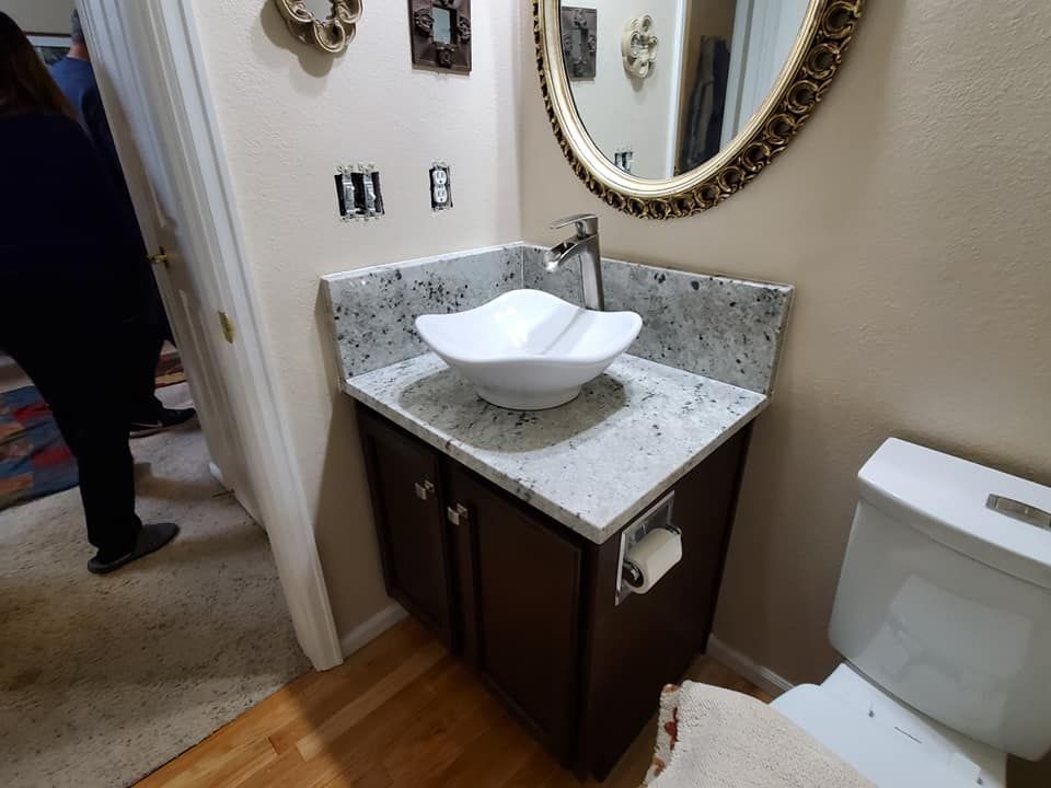 Bathroom with white vessel sink, dark brown cabinet, granite countertop, and oval mirror.