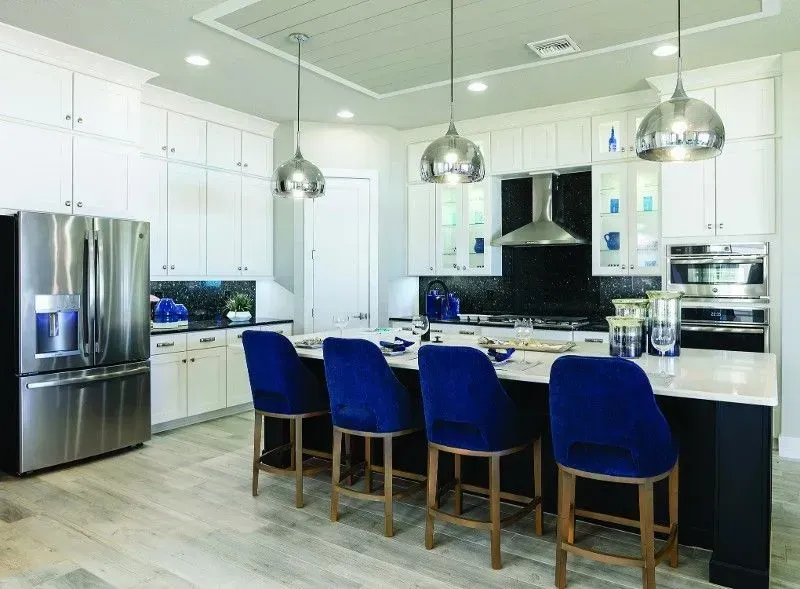 Modern kitchen with white cabinets, dark island with blue chairs, stainless steel appliances.