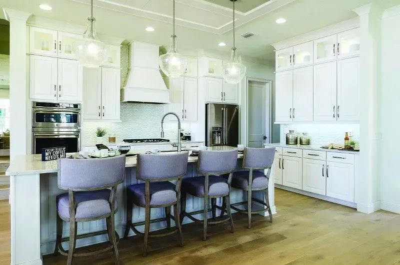 White kitchen with island, bar stools, stainless steel appliances, and glass globe pendant lights.