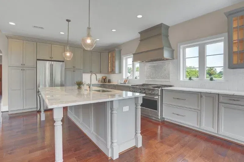 Spacious, modern kitchen with gray cabinets, marble countertops, stainless steel appliances, and wood floors.