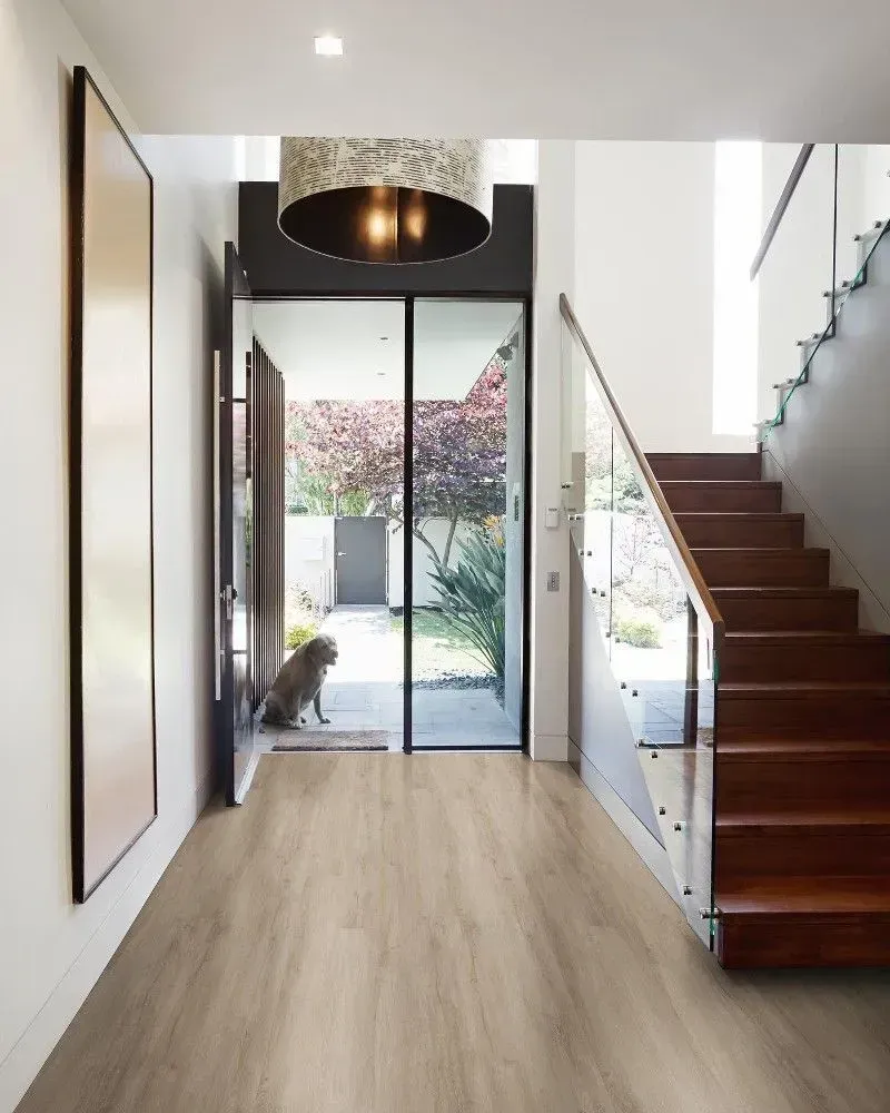 Hallway with wood floors, stairs, and a dog at the door.