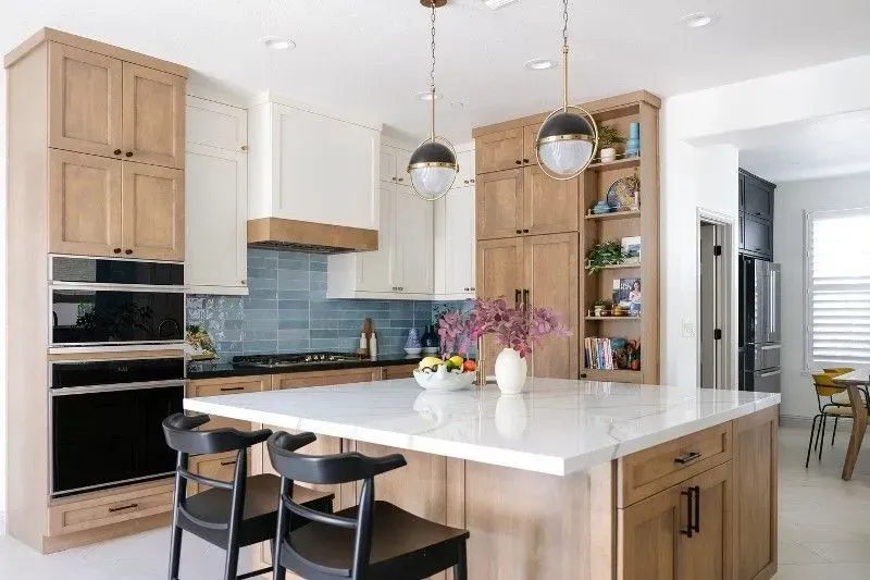 Kitchen with wood and white cabinets, island with stools, and blue tile backsplash.