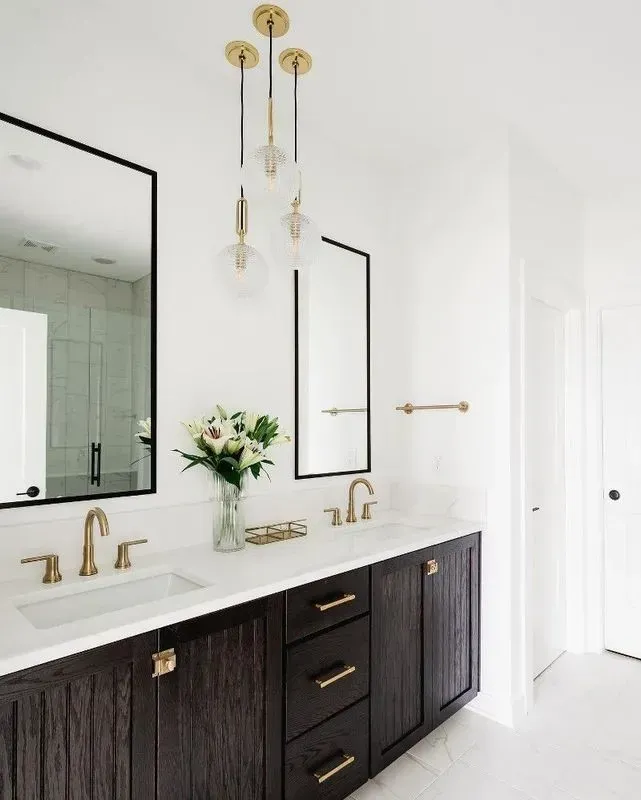 Modern bathroom with dark wood vanity, gold fixtures, white countertop, mirrors, and pendant lights.
