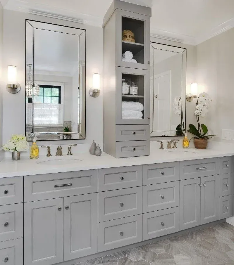 Gray bathroom vanity with tall cabinet, mirrors, sconces, and countertop with sinks.