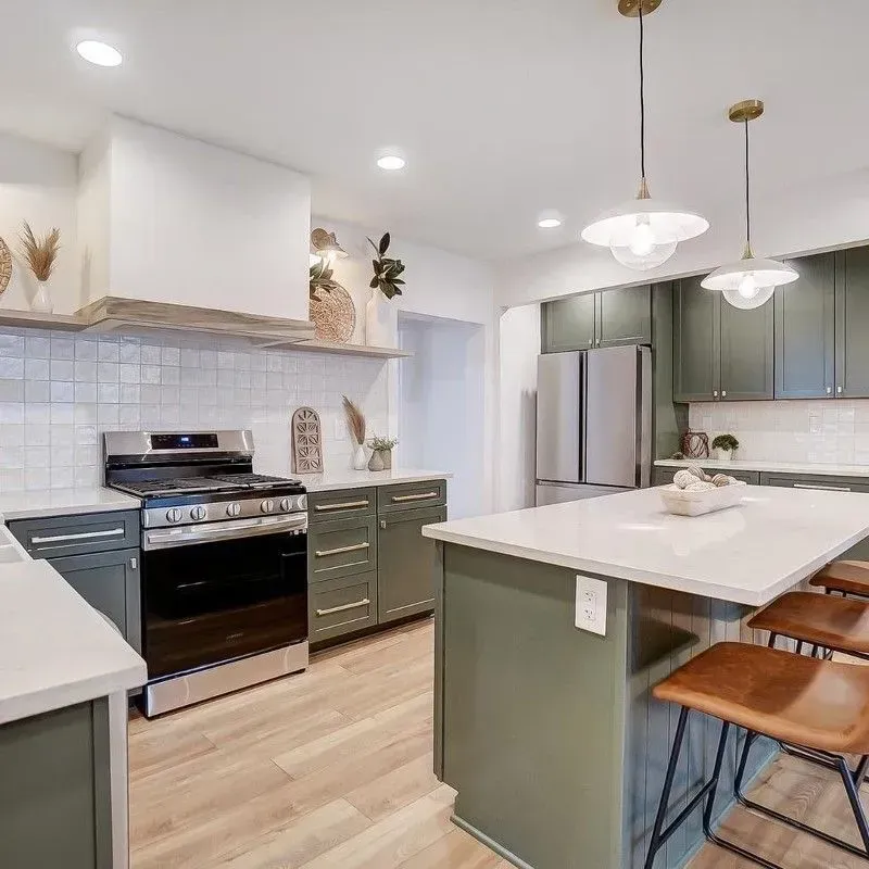 Modern kitchen with green cabinets, white countertops, and wood flooring; island with bar stools.