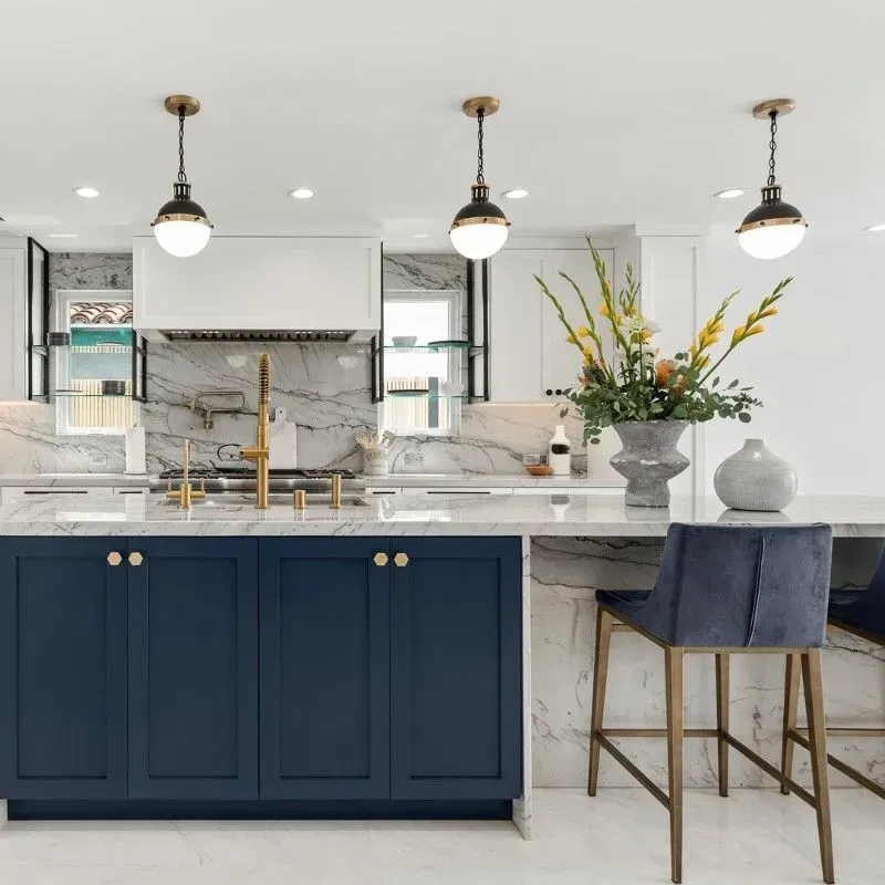Modern kitchen with blue island, marble countertops, brass fixtures, and pendant lights.
