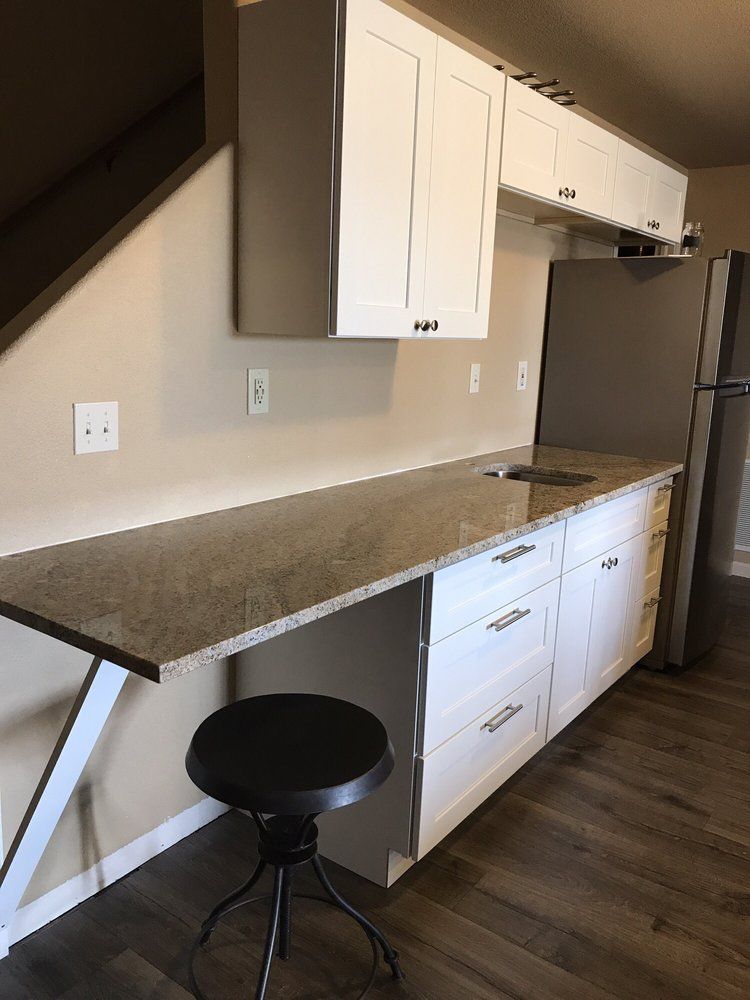 A small kitchenette with white cabinets, a granite countertop, and a stainless steel refrigerator.