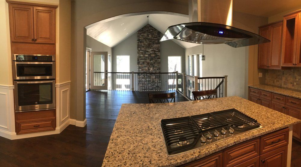 Kitchen with island, dark wood cabinets, stainless steel appliances, and view of a living area with stone fireplace.