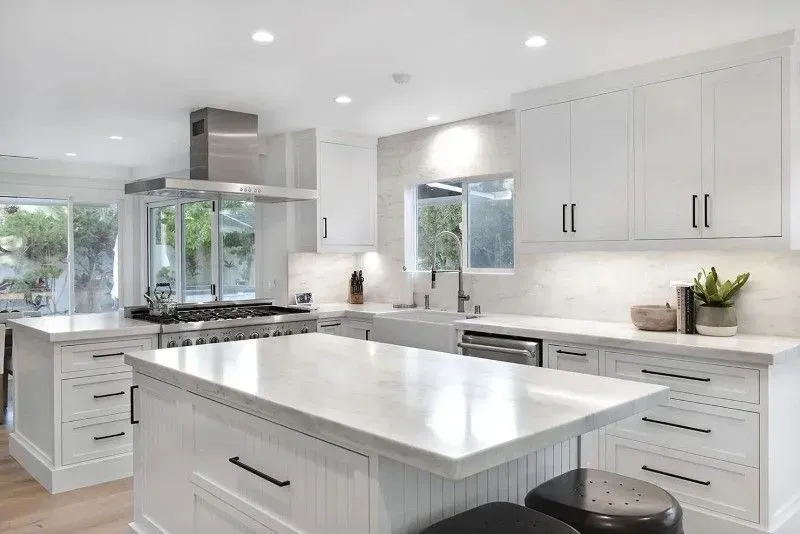 White kitchen with island, cabinets, stainless steel range hood, and large windows.