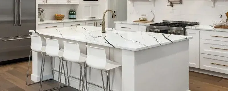 Modern white kitchen with island, quartz countertop, and white bar stools.